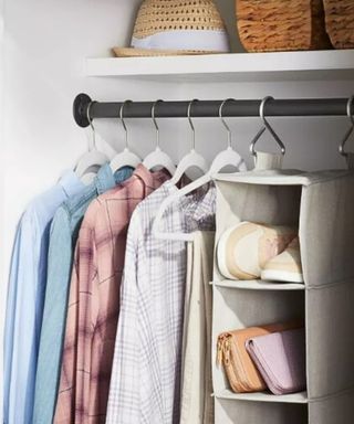 A white closet with a clothes rod with shirts on it, gray clothes organizer, and shelf with a hat on it - Shortcut