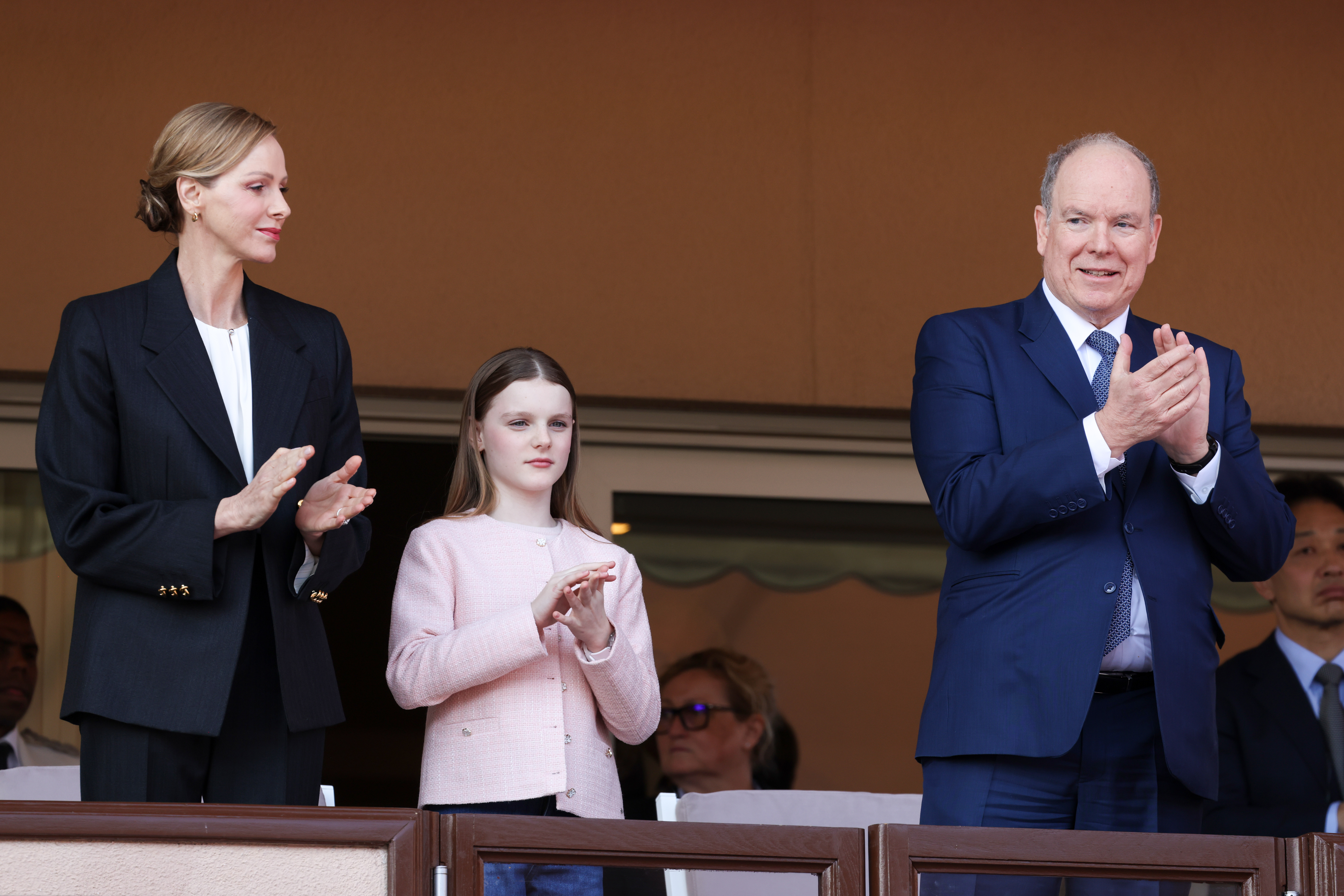Princess Charlene, Princess Gabriella and Prince albert wearing blazers and clapping at a rugby match