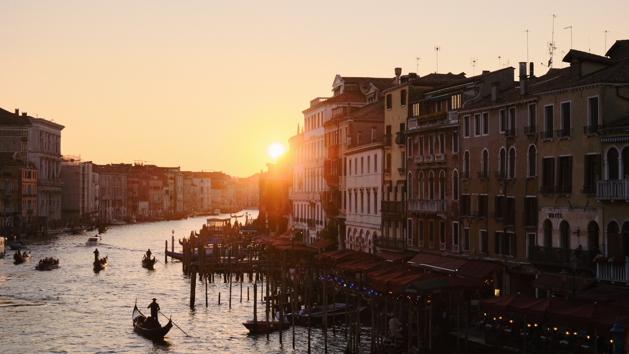 sunset scene with people on gondolas on canals of Venice as the sky glows golden.