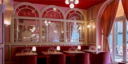 A retro-futuristic hotel restaurant features red and rose-tinted dazzling decor, including mirrored arched walls, plush velvet seating, Art Deco accents, and more.