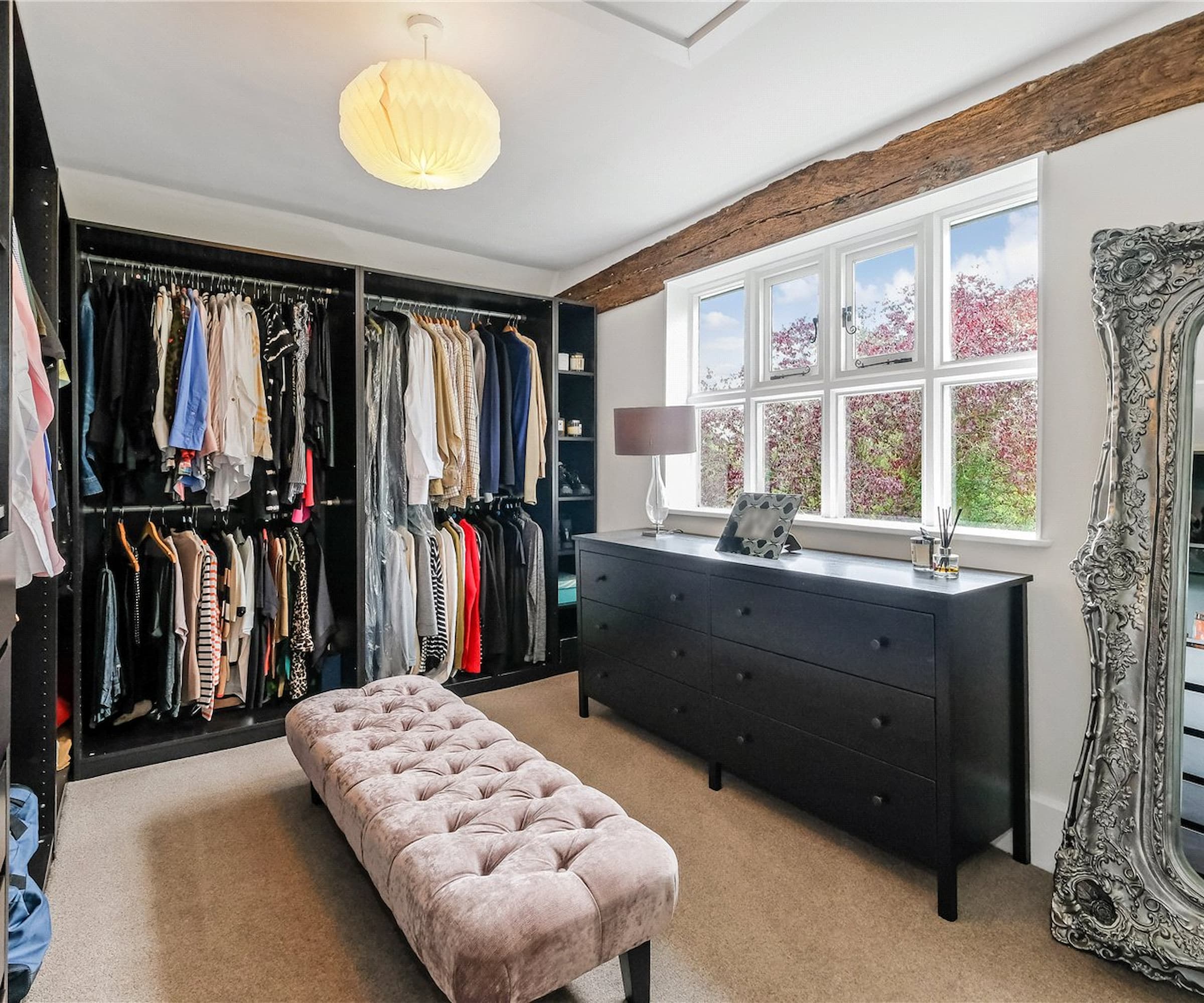 A walk-in wardrobe with black wardrobes and an oak beam in the ceiling and large windows