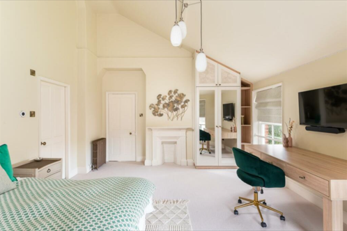 A white bedroom with desk opposite the bed and a slanted roof