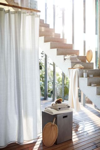 a white shower curtain by H&M Home in an indoor/outdoor bathroom, with a staircase in the background