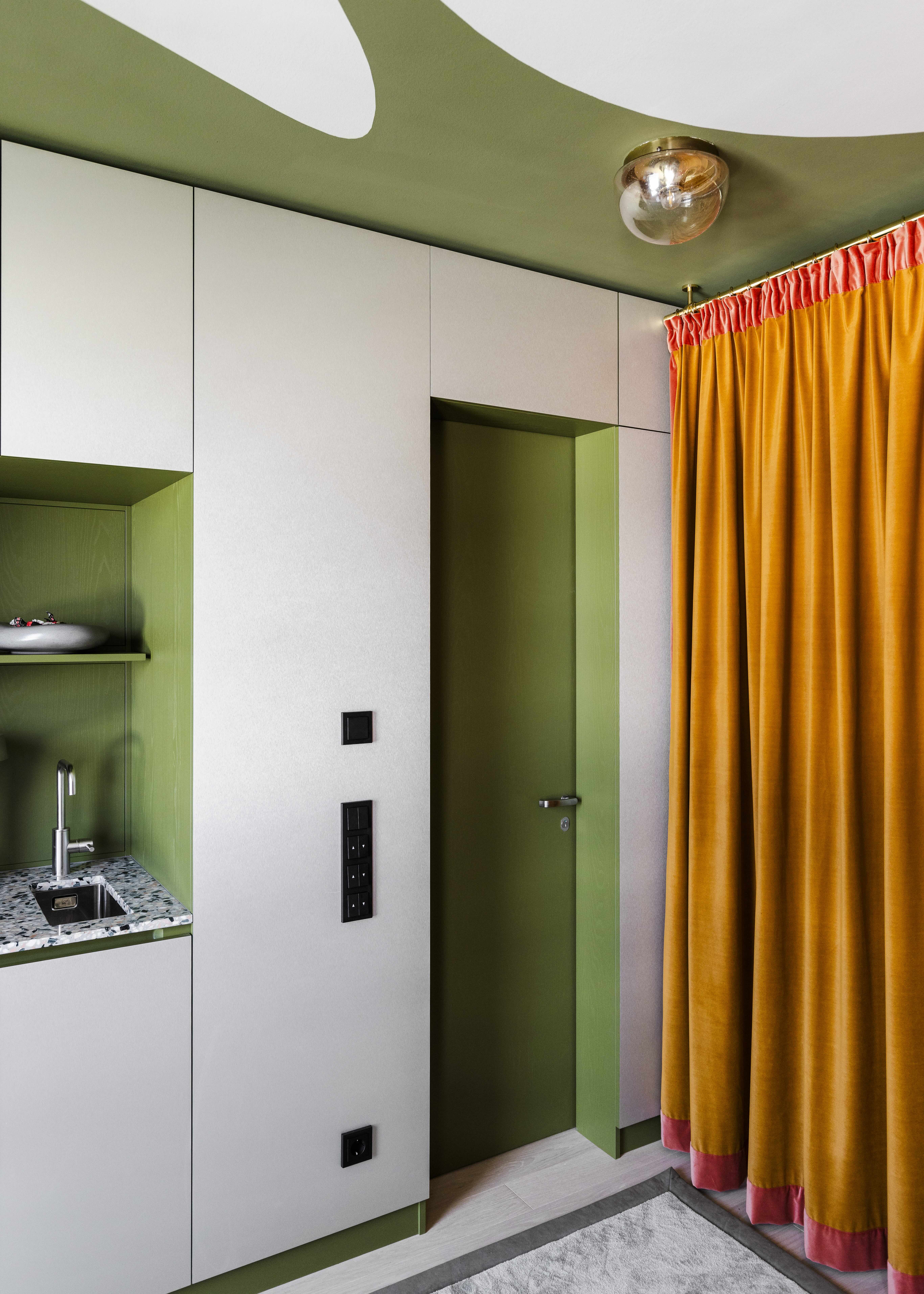 A contemporary green kitchen and entryway with bright orange and salmon pink curtain