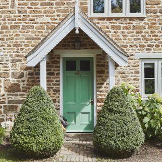 Light stone house with green front door and bushes outside.