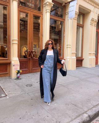 @raeannlangas wearing overalls and a long black coat in NYC.