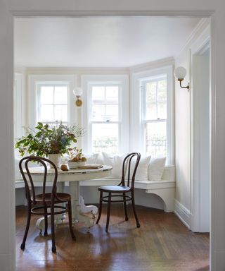 A white dining nook with a round distressed table and dark wood chairs