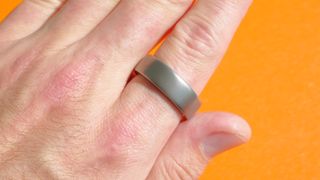 A close up of the Amazfit Helio Ring on a user's finger against a colorful background