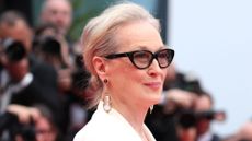 Meryl Strepp pictured on the red carpet at Cannes with her hair in a chignon, a white jacket and tinted cat eye glasses