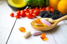 Best multivitamin: tablets on side sitting on wooden spoon with fruit surrounding
