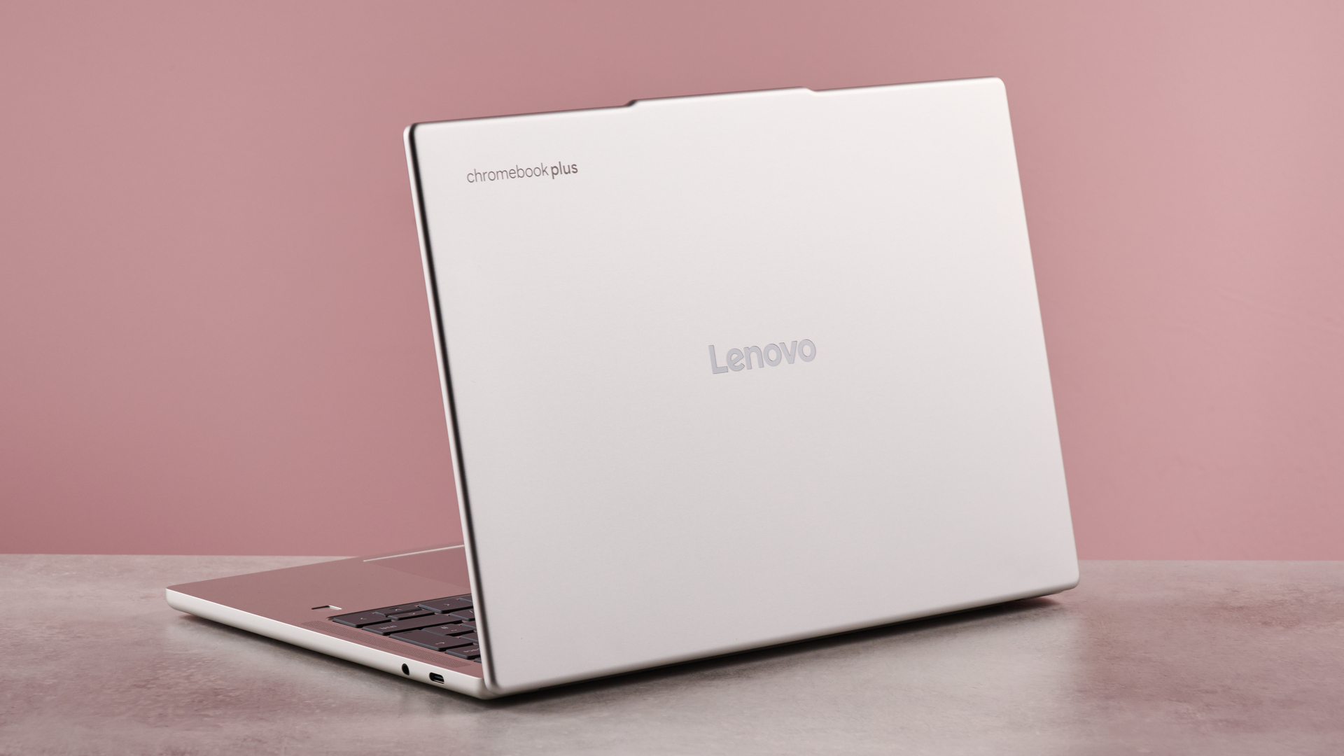 Back of Lenovo Chromebook Plus 14-inch, open on desk with pink background