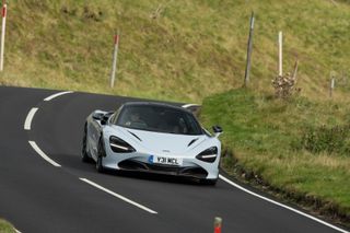 A white McLaren driving on the right side of the road.