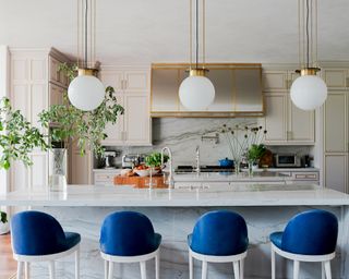 A kitchen with a marble island, warm grey cabinets and blue breakfast bar chairs