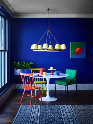inky blue dining room with bright yellow pendant, bright artwork, colorful chairs, marble round table