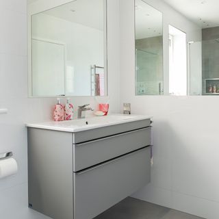 A grey vanity unit with pink accessories and mirror on the wall