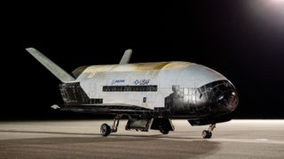 a black-and-white space plane sits on a runway at night.