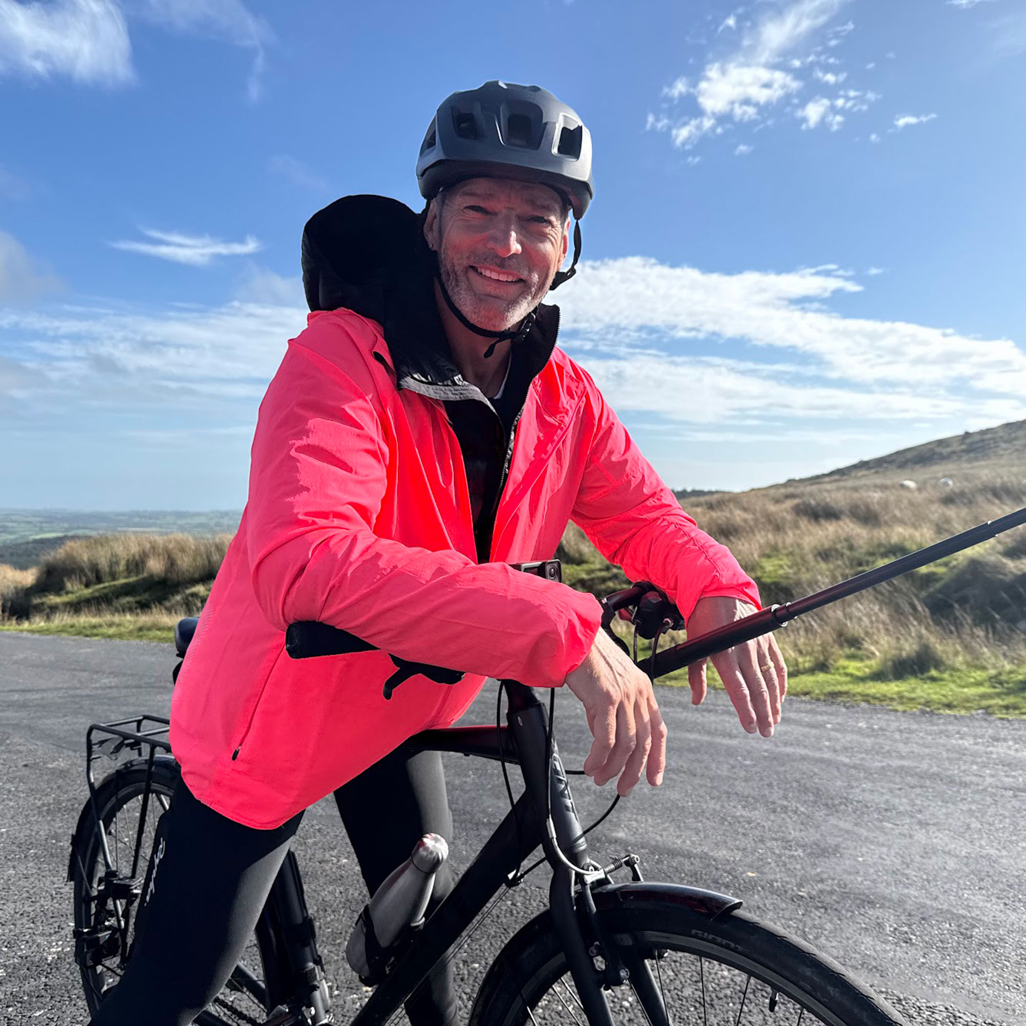 Fred Sirieix in pink flourescent jacket on a black bike in the countryside