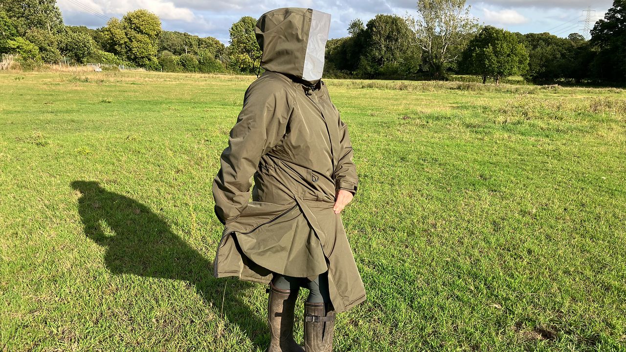 Lady wears Reincoat Pro in a field, showing reinshield feature viewed from the side