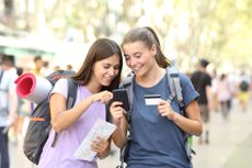 Two traveling teen girls check their credit card and phone.