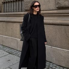 Annabel wears a black long coat, black sweater, and black trousers.