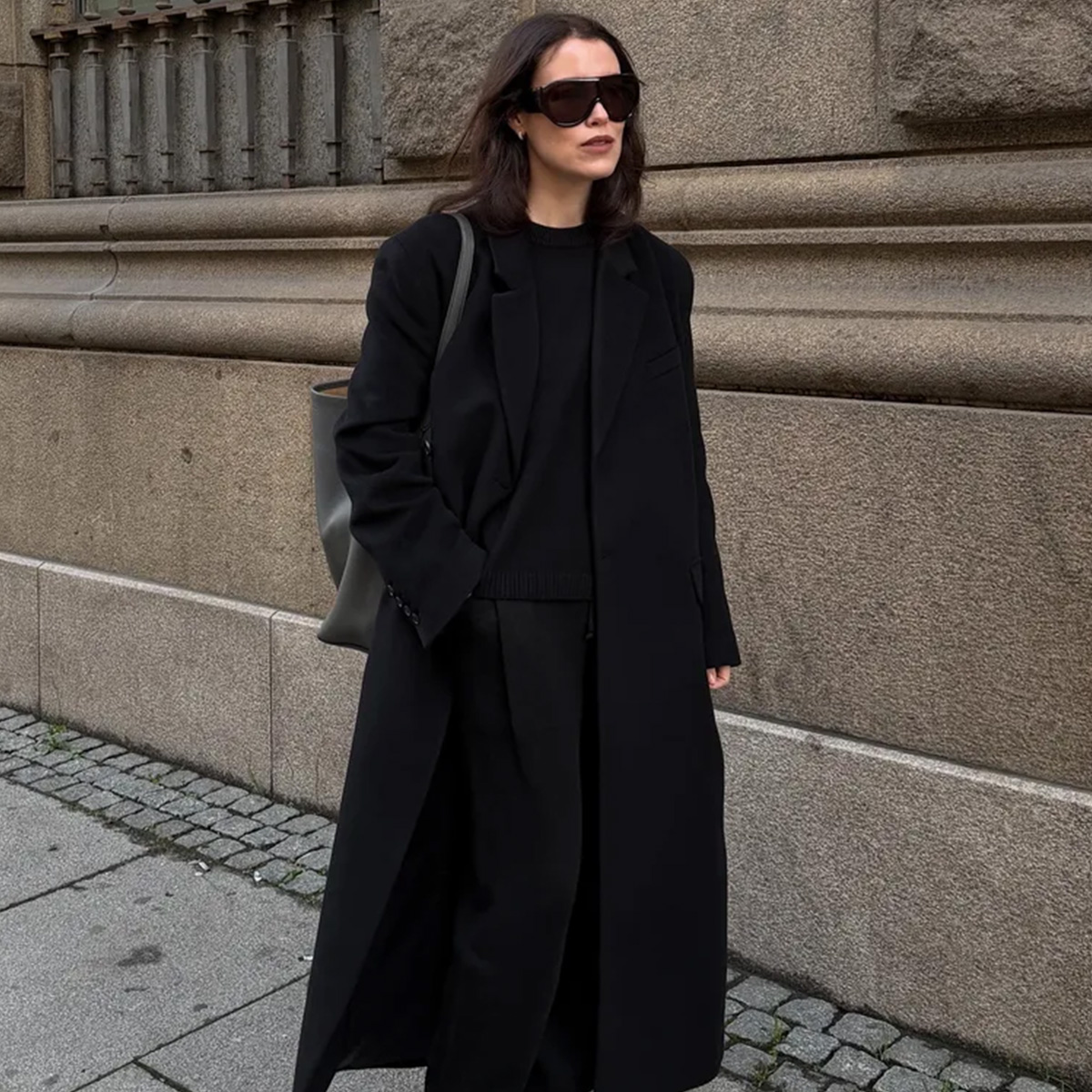 Annabel wears a black long coat, black sweater, and black trousers.