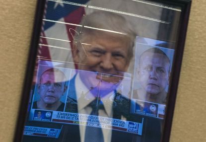 Mugshots of bombing suspect Cesar Sayoc are reflected on a portrait of President Trump prior to a press conference at the Department of Justice in Washington, DC on October 26, 2018.