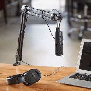 A boom mic stand from Audio-Technica holds a mic near a laptop for podcast recording.