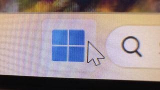 A close-up photo of a monitor displaying the Windows 11 start icon, with the screen's pixels clearly visible