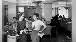 Two women talking by a water cooler in a 1940s office