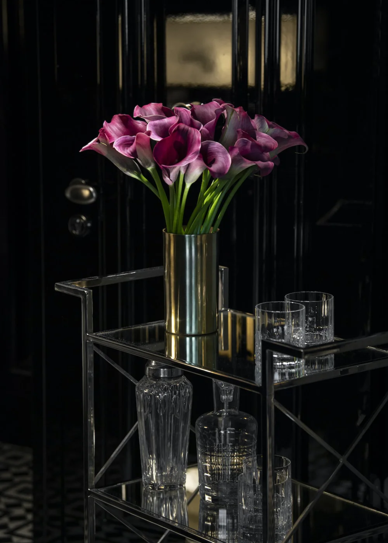 A vase of purple calla lilies in a gold vase on a bar tray