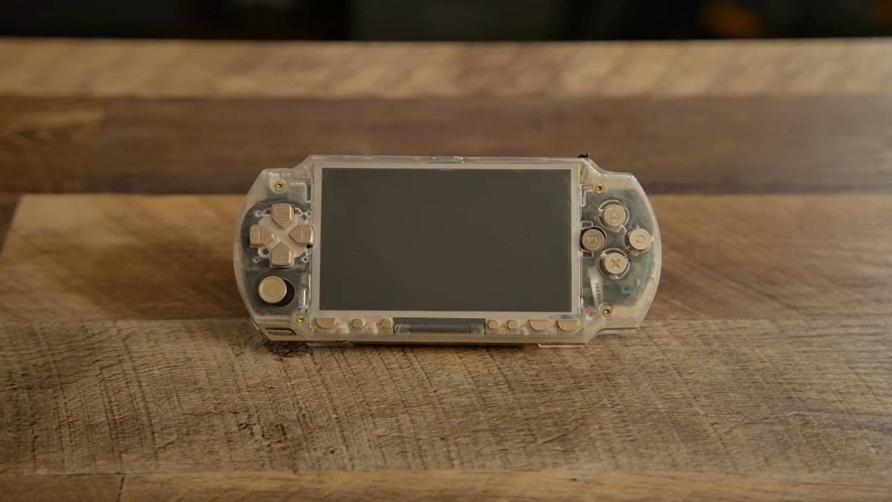 Brass and acrylic PSP sitting on woodgrain desk.