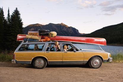 Family travelling in a car with a canoe strapped to the roof