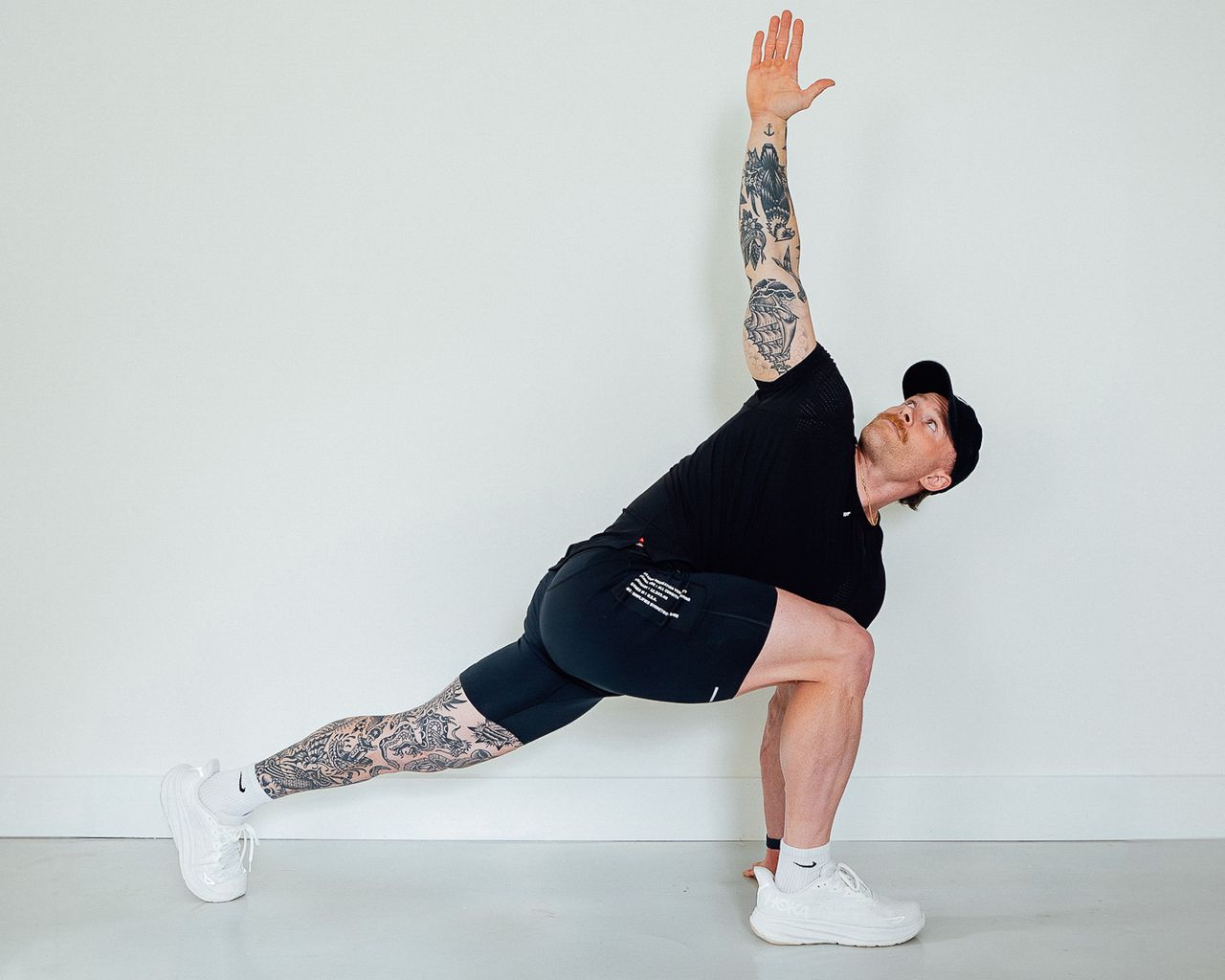 Coach Corey Perkins performs the world's greatest stretch. His legs are in a low lunge position, with his right leg forward. His left hand rests on the floor next to his right foot and his right hand is held straight up in the air.