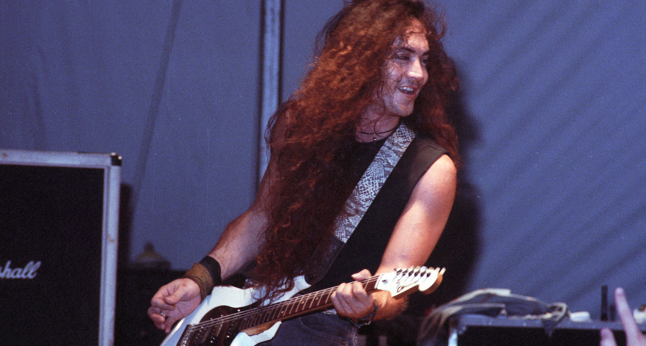 Jake E. Lee smiles as he performs live with Badlands, playing his customary white Charvel.