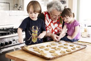 A grandmother helping her young grandchildren - a boy and girl - bake cookies in her home.