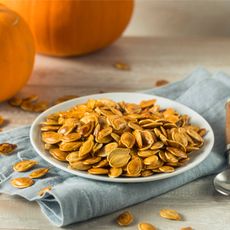 Plate of roasted pumpkin seeds with pumpkins in background