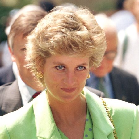 Princess Diana wears a bright green jacket with a matching polka-dot shirt underneath and has short blonde coiffed hair, a bag with a gold chain strap, and she's wearing black eyeliner