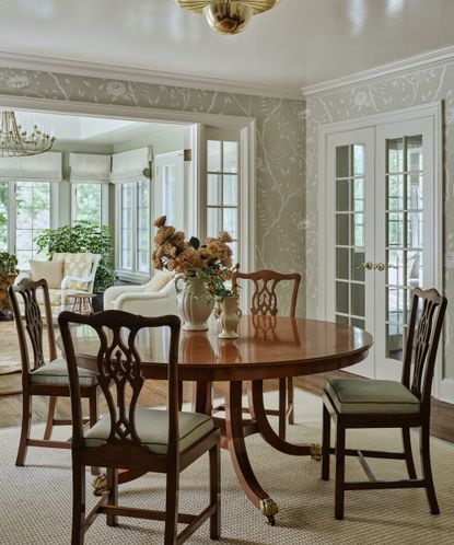a soft green floral wallpapered dining room with french doors and antique wooden furniture