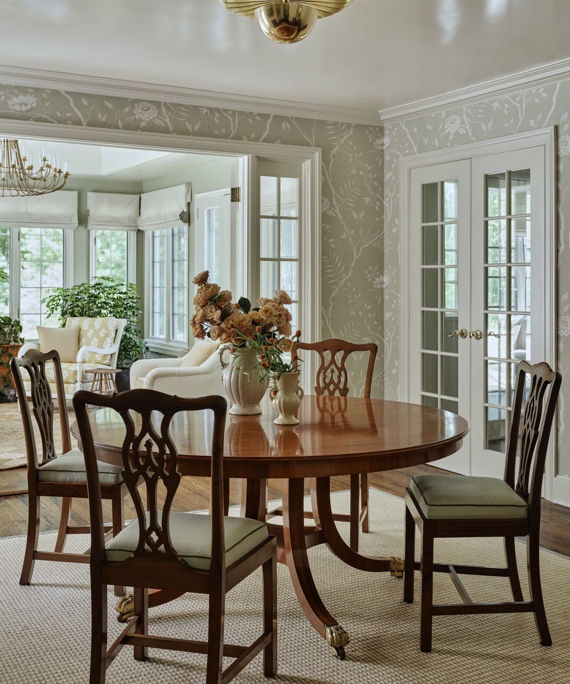 a soft green floral wallpapered dining room with french doors and antique wooden furniture