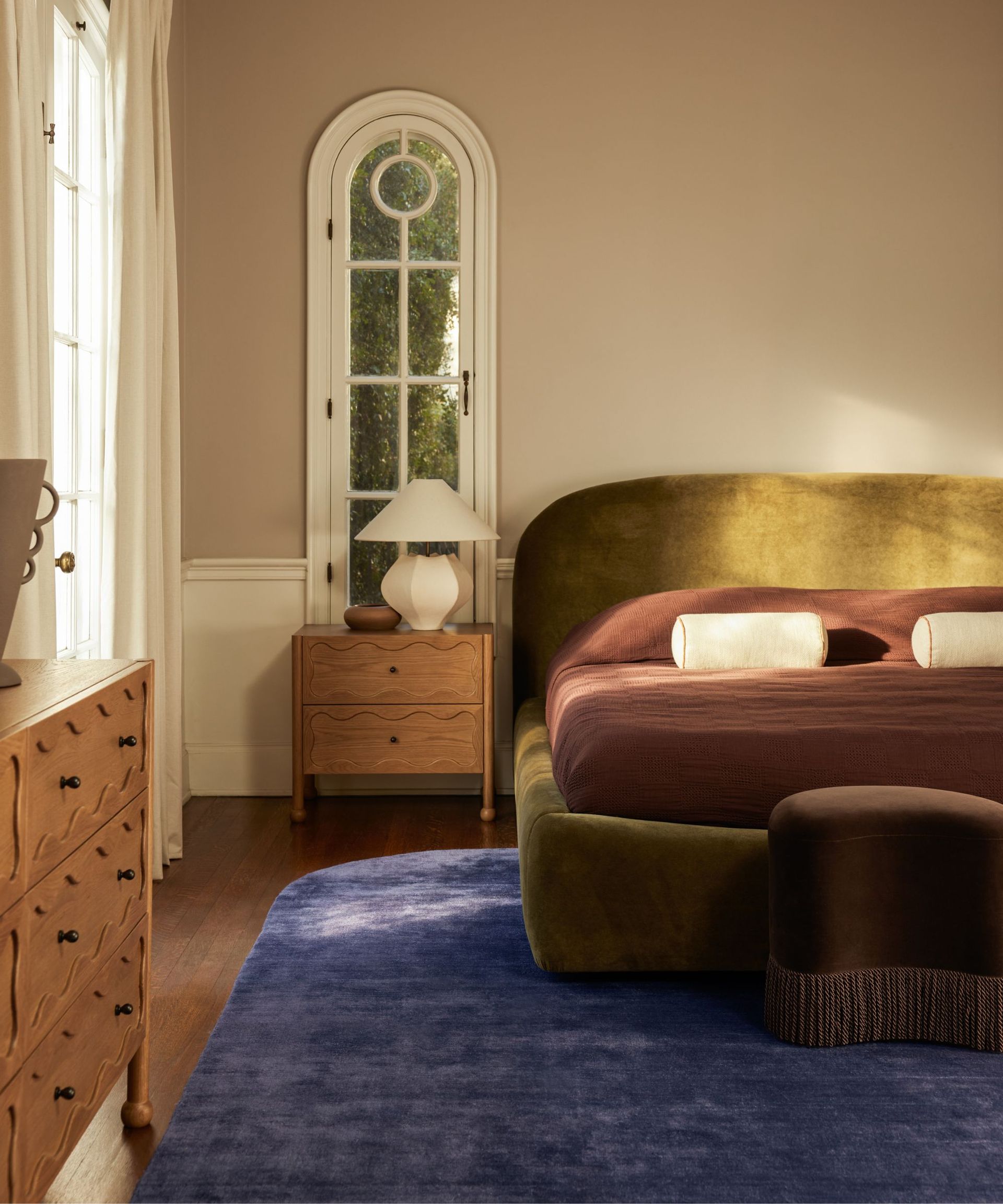 earthy bedroom of aimee song styled with her lulu and georgia collaboration with an indigo purple blue rug, a green velvet bed and purple bedding with wavy detailed wooden furniture