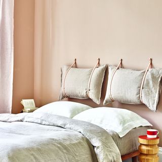 A bedroom with walls painted in soft peach and with a pillow headboard above the bed