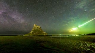 Photograph of Lindisfarne Castle at night with the band of the Milky Way on the left of the image and a streaking line of green light on the right hand side