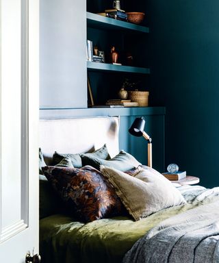 bedroom with dark blue walls, shelving, neutral headboard and cushions