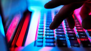 A close up shot of someone pressing a keyboard key on a laptop covered in blue and red lighting