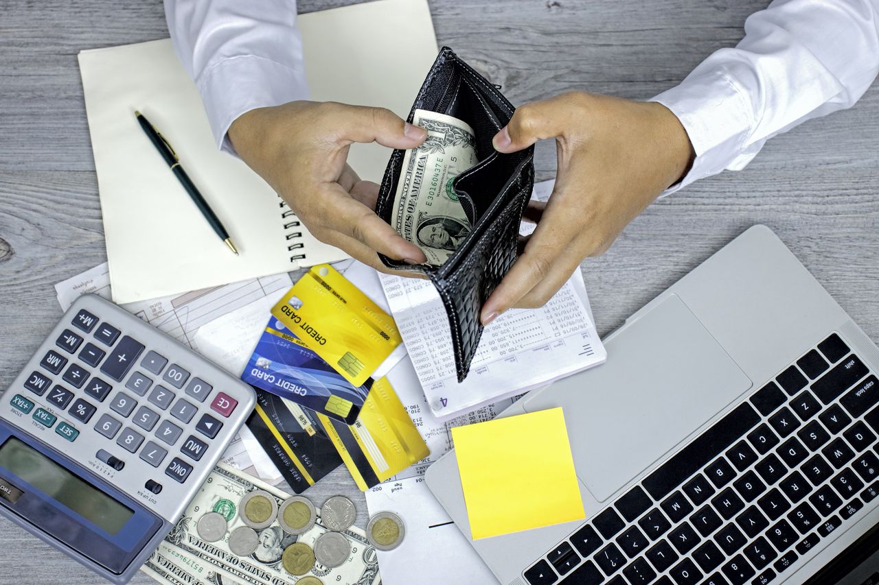 Man opening wallet, with debt expense bills and credit cards, at a table. 