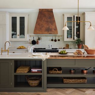 sage green and white kitchen, wooden floor, copper cooker hood, white work tops, kitchen storage