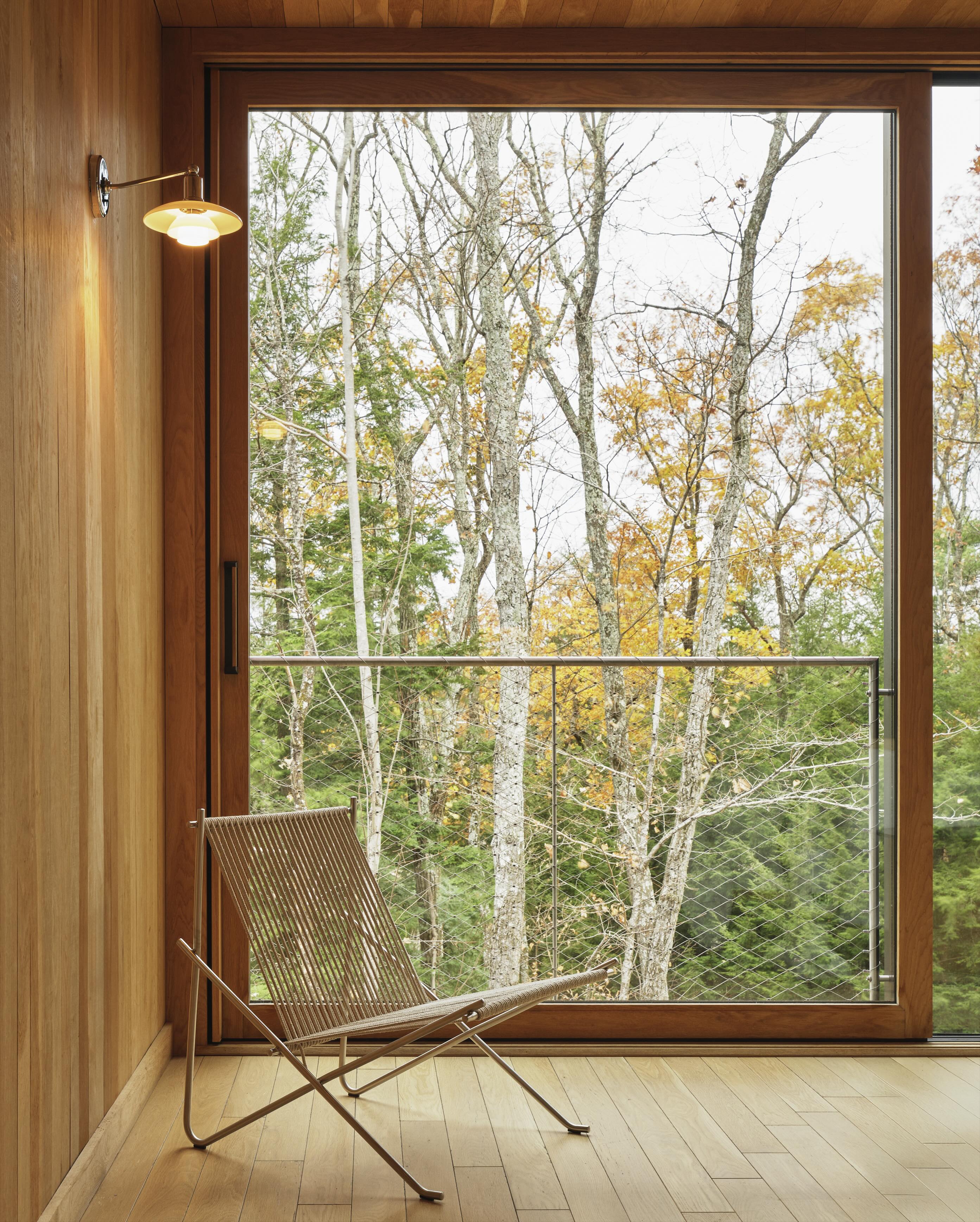 A corded chair with a metal frame sits in front of a window with forest in the background.