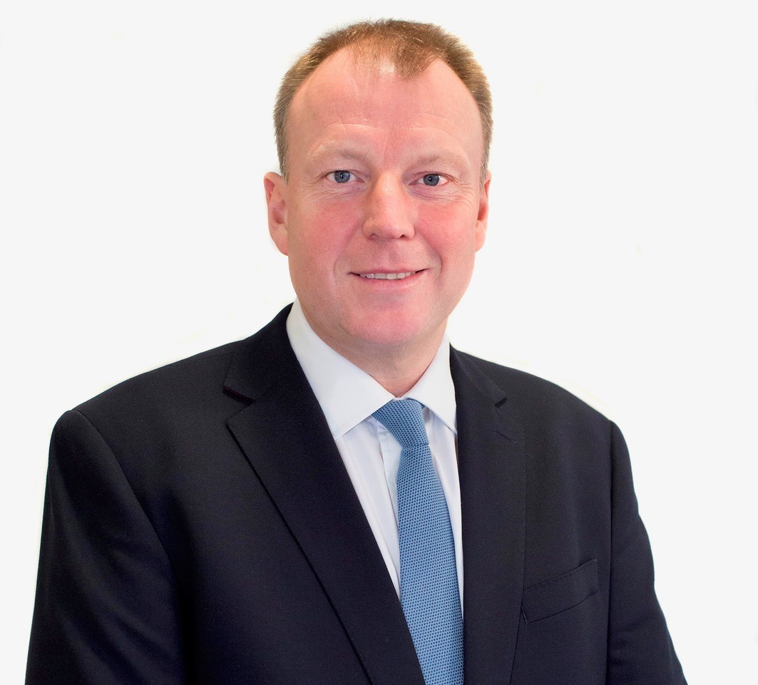 A man with a white shirt and light blue tie with a navy suit jacket