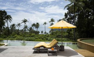 Soneva Kiri exterior view of pool with loungers and umbrella, forest in background