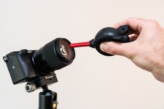 A hand using a blower to clean a camera lens